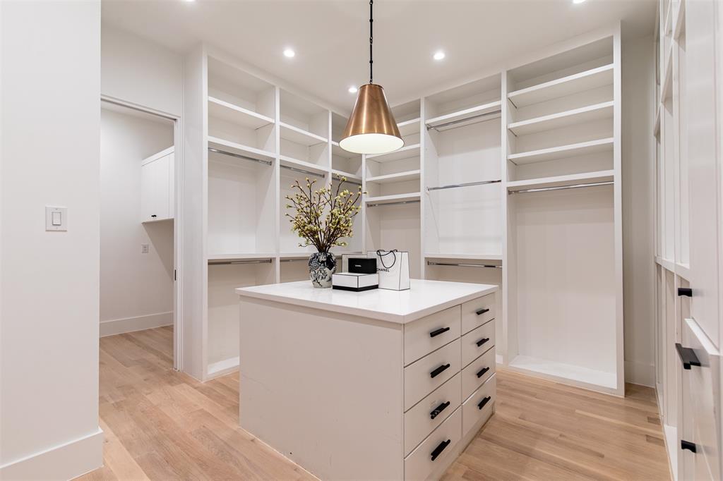 Custom floor-to-ceiling built-in cabinetry with integrated shelving and hanging rods, center island with stone countertop, multi-drawer storage, recessed lighting, and wood-finish flooring