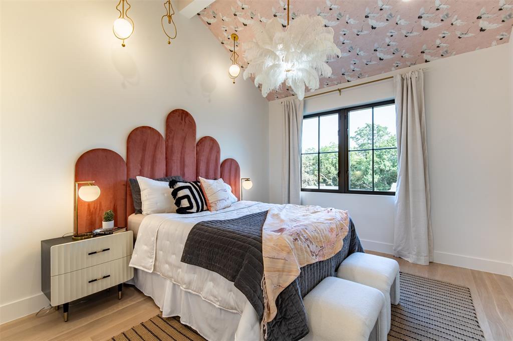 Vaulted ceiling with patterned wallpaper treatment, wood-finish flooring, multi-pane black-framed windows, and statement pendant lighting
