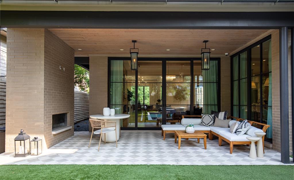 Covered patio featuring a checkered tile floor, brick fireplace, wood-plank ceiling, and expansive metal-framed glass sliding doors