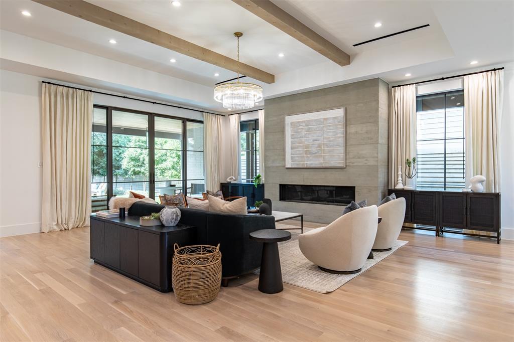 Living room featuring wood-finish flooring, exposed ceiling beams, a floor-to-ceiling textured stone fireplace surround, recessed lighting, and expansive floor-to-ceiling windows