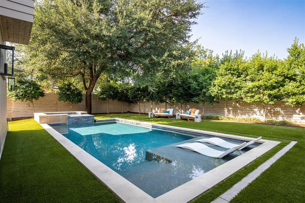 Private backyard featuring a swimming pool with a tanning ledge and integrated spa, surrounded by synthetic turf and horizontal wood fencing