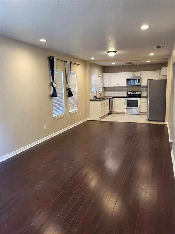 Dark wood-finish flooring, recessed lighting, white cabinetry, stainless steel appliances, and subway tile backsplash