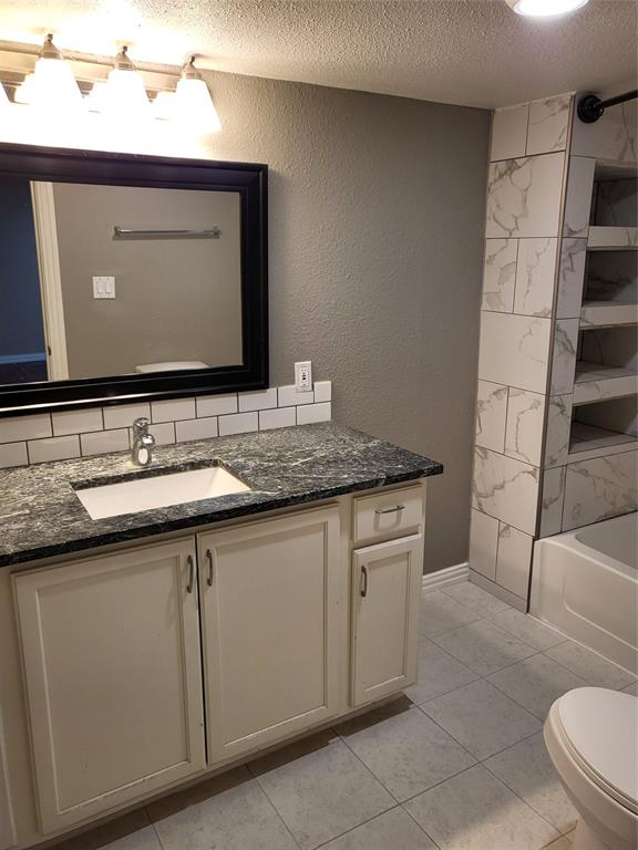 Bathroom featuring a vanity with stone-finish countertop, integrated basin, subway tile backsplash, and built-in shelving with stone-look tile surround