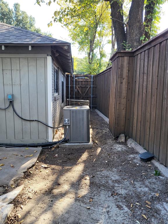 Exterior side yard featuring vertical siding, masonry wall construction, a dedicated HVAC unit on a concrete pad, and full-height wood fencing