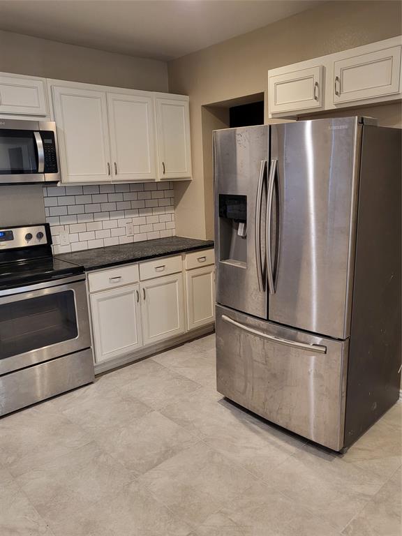 Kitchen featuring white shaker-style cabinetry, stainless steel appliances, subway tile backsplash, dark stone-finish countertops, and large-format tile flooring