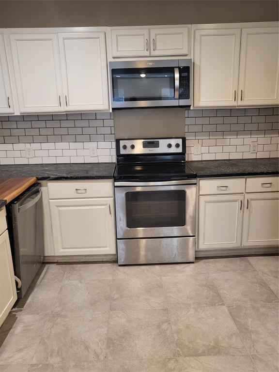 Kitchen featuring white shaker-style cabinetry, dark stone-finish countertops, stainless steel appliances, subway tile backsplash, and neutral-tone tile flooring