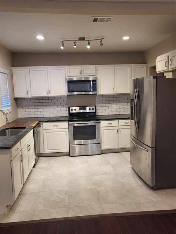 Kitchen featuring white shaker-style cabinetry, dark stone countertops, stainless steel appliances, subway tile backsplash, and ceramic tile flooring