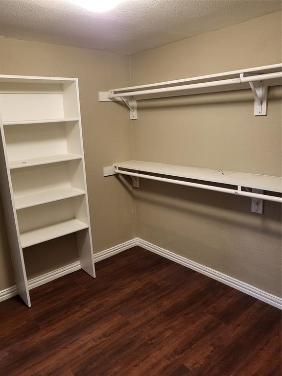 Storage area featuring wood-finish flooring, white built-in shelving unit, and dual tiers of wall-mounted hanging rods