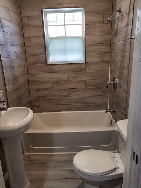 Bathroom featuring floor-to-ceiling plank-style wall tiling, pedestal sink, built-in bathtub with shower head, and wood-finish flooring