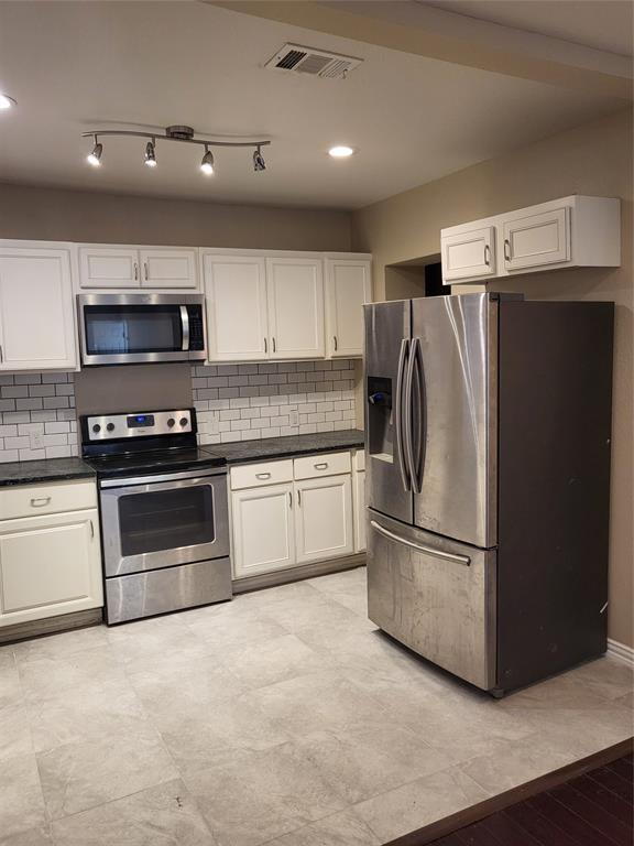 Kitchen featuring white shaker-style cabinetry, stainless steel appliances, dark stone countertops, subway tile backsplash, and large-format tile flooring