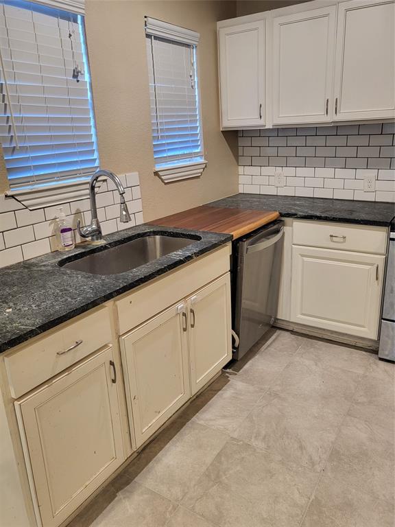Kitchen featuring white cabinetry, dark stone countertops, wood-finish countertop section, stainless steel under-mount sink with pull-down faucet, and subway tile backsplash