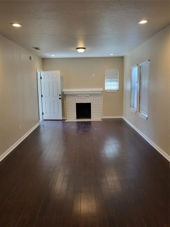 Wood-finish flooring, white brick fireplace with a mantle, recessed ceiling lighting, and multiple windows with horizontal blinds