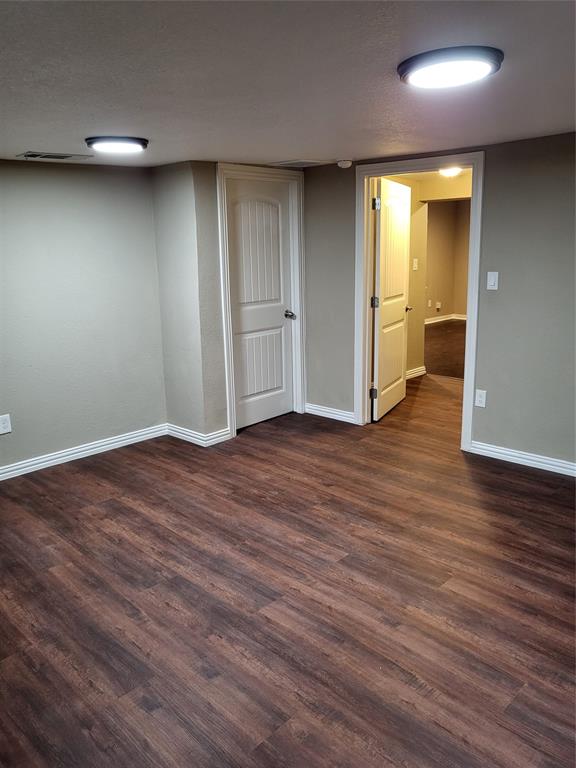 Interior space featuring dark wood-finish flooring, neutral wall paint, two-panel interior doors, and flush-mount circular lighting fixtures