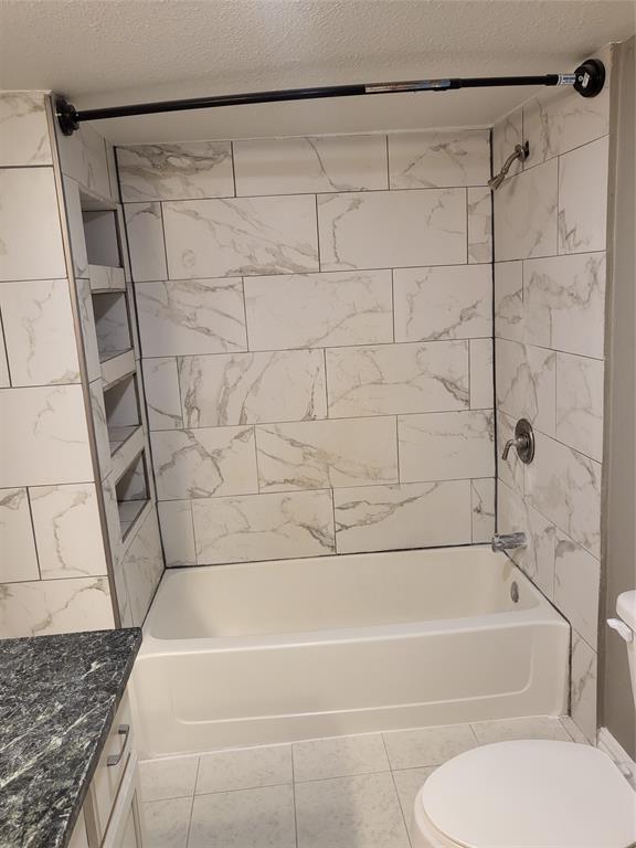 Bathtub surround featuring large-format neutral-toned tile with veining, integrated wall shelving, and metal shower fixtures