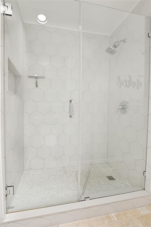 Glass-enclosed shower with white hexagon wall tiles, circular floor tiles, and a built-in shower niche