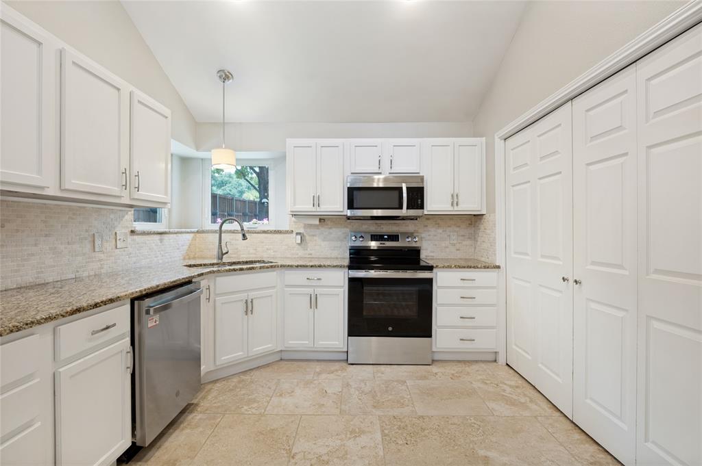 Bright, open kitchen featuring white cabinetry, stainless steel appliances, granite countertops, tile backsplash, and stone-finish flooring