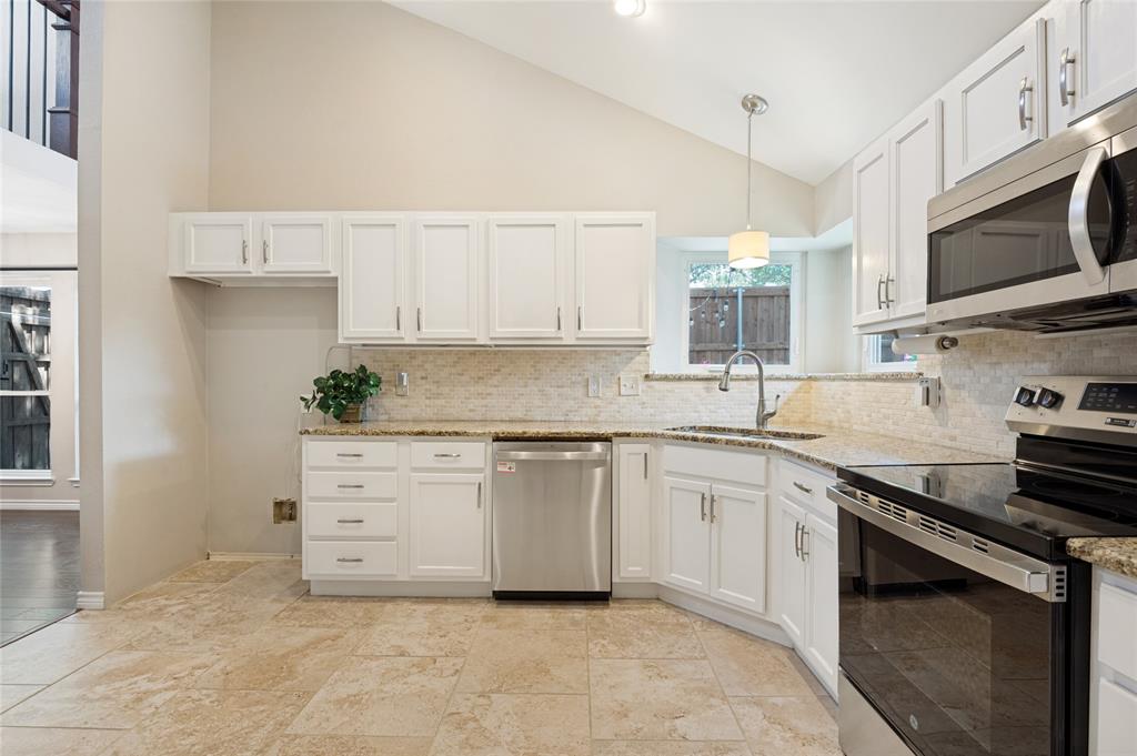 Vaulted ceiling kitchen featuring white cabinetry, granite countertops, stainless steel appliances, and tile flooring
