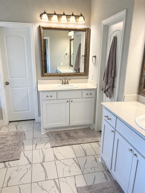 Primary bath with dual vanities and tile flooring.