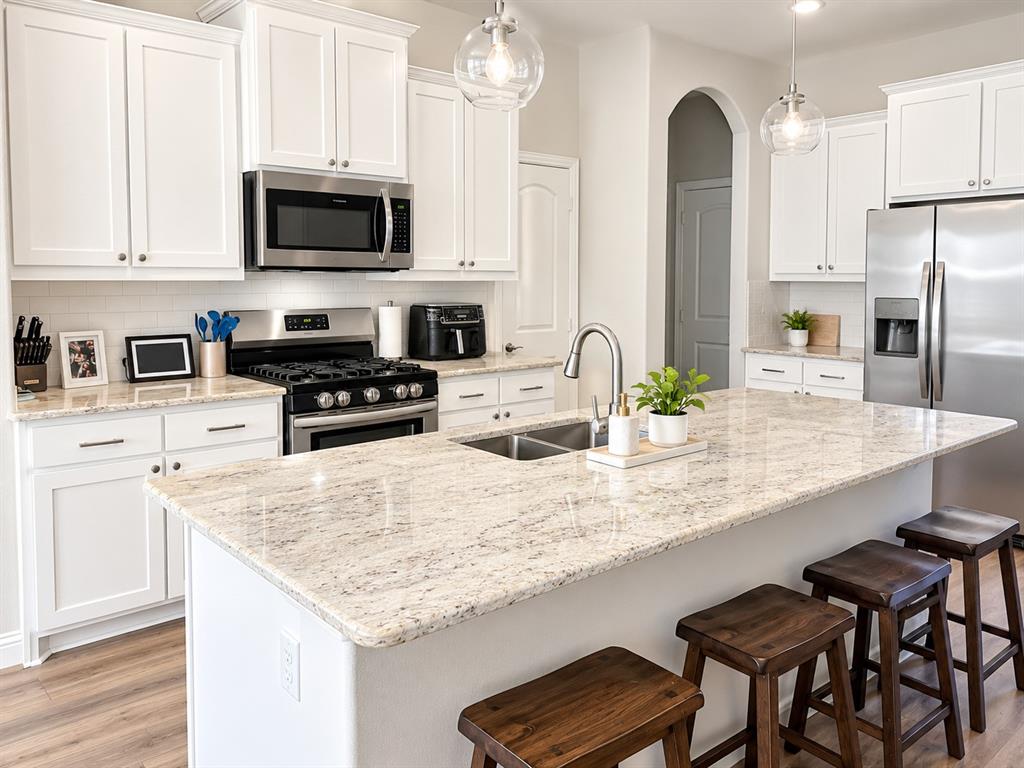 Bright kitchen with white cabinetry, stainless steel appliances, and a large island with bar seating under pendant lights.