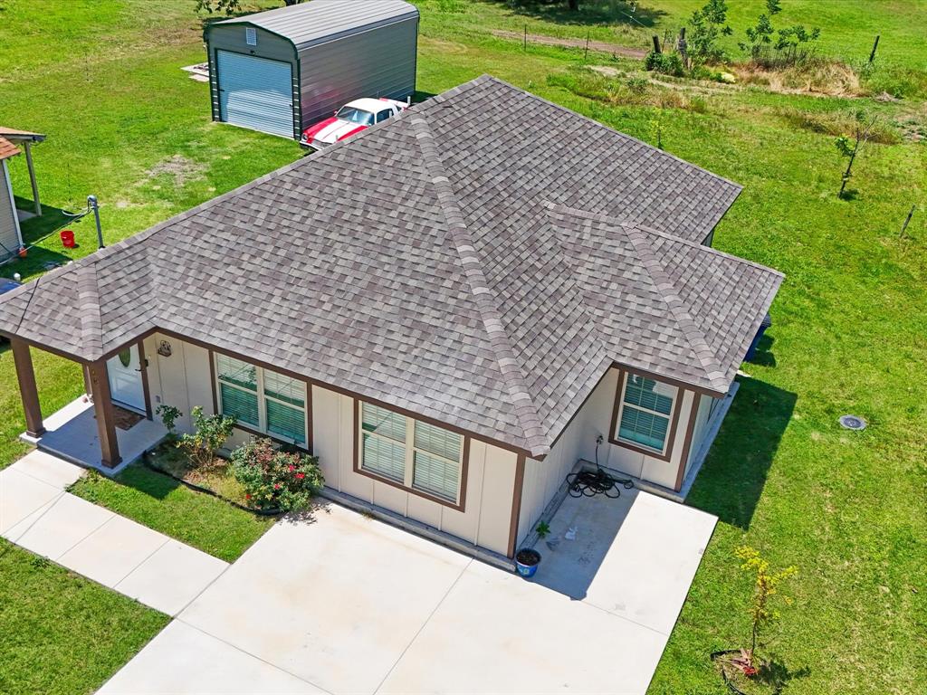 Exterior featuring an asphalt shingle roof, concrete driveway, covered front entryway, and a detached metal storage structure situated on a grass-covered lot