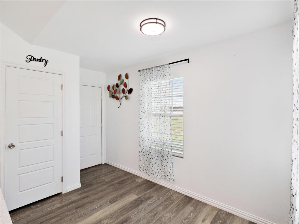 Wood-finish flooring, two solid-core interior doors, single-pane window with horizontal blinds, and a flush-mount circular ceiling light fixture