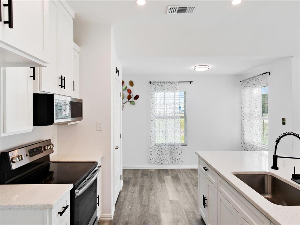 Kitchen featuring white cabinetry with matte black hardware, stone-finish countertops, stainless steel appliances, a gooseneck faucet with a single-basin undermount sink, and wood-finish flooring