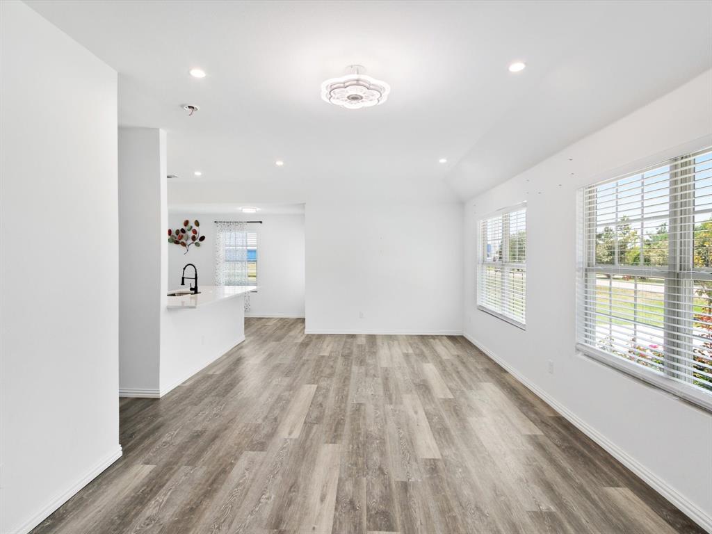 Open-concept interior featuring wood-finish flooring, recessed lighting, a central decorative ceiling fixture, and large windows with horizontal blinds