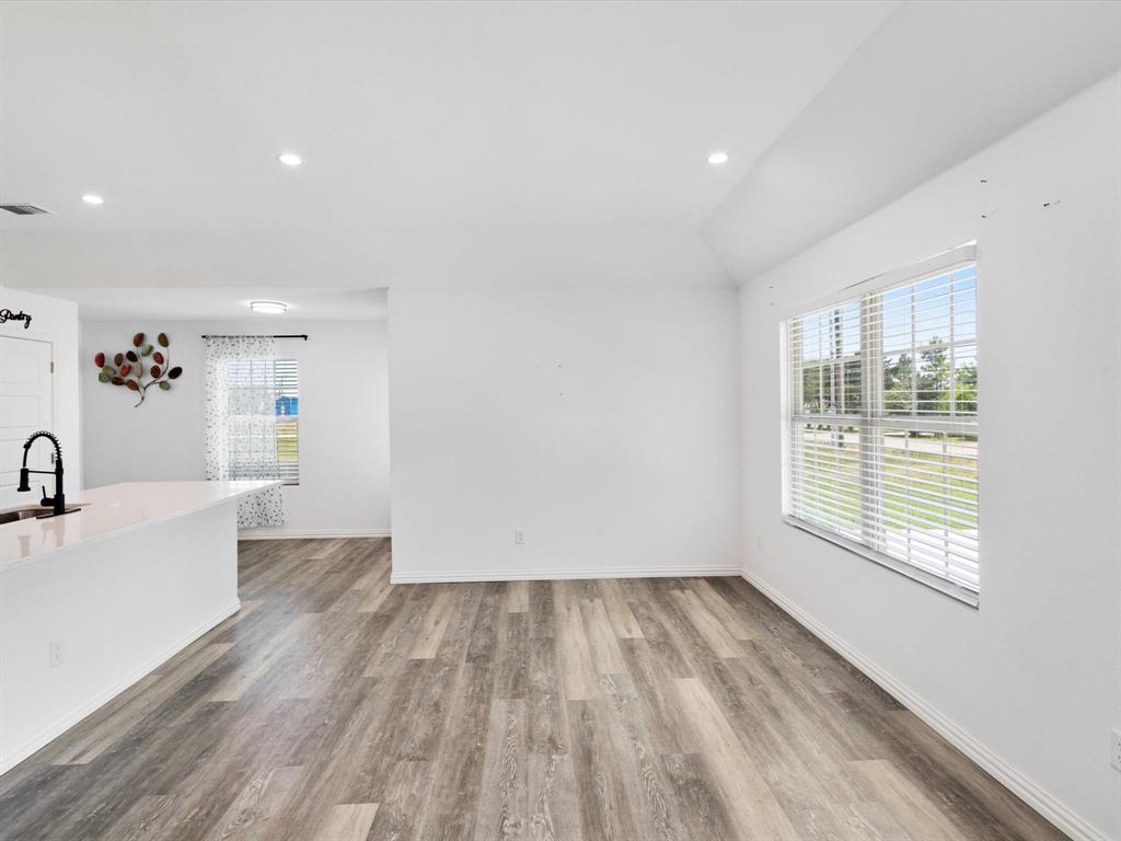Interior space featuring wood-finish flooring, recessed lighting, high ceilings, large windows with horizontal blinds, and a kitchen counter with an integrated sink and matte black faucet