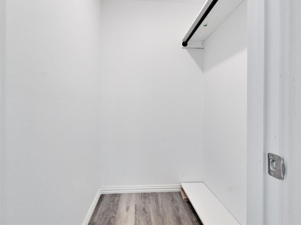 Storage space featuring wood-finish flooring, a built-in shelf, and a mounted hanging rod