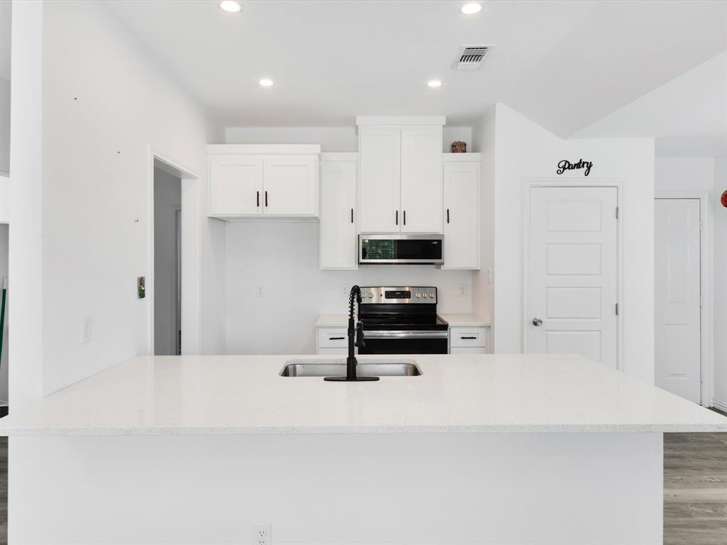 Kitchen featuring white cabinetry, quartz countertops, a stainless steel over-the-range microwave, a black pull-down faucet, and recessed lighting