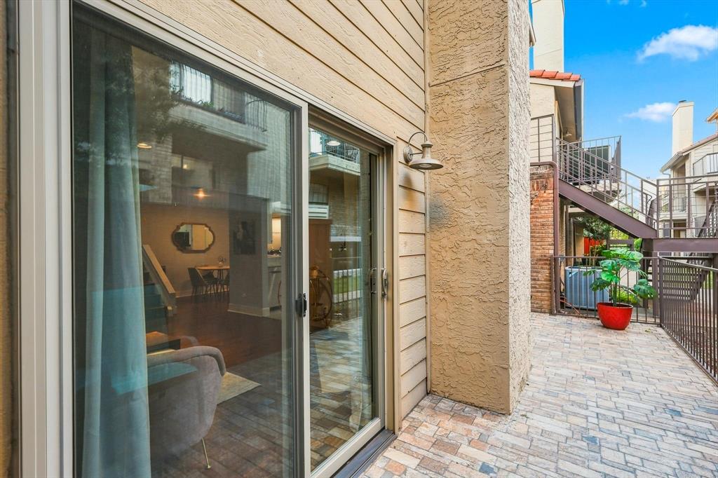 Private patio featuring stone-paver flooring, horizontal lap siding, brick accent wall, and exterior gooseneck lighting