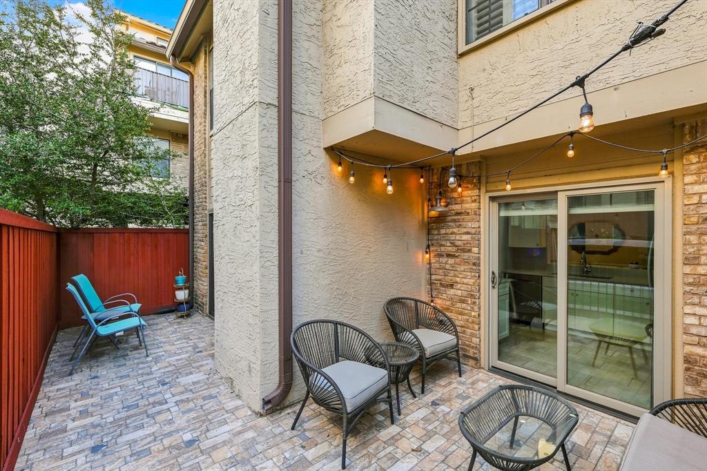Private patio featuring multi-toned stone paver flooring, a red privacy fence, and brick and stucco exterior walls with sliding glass door access