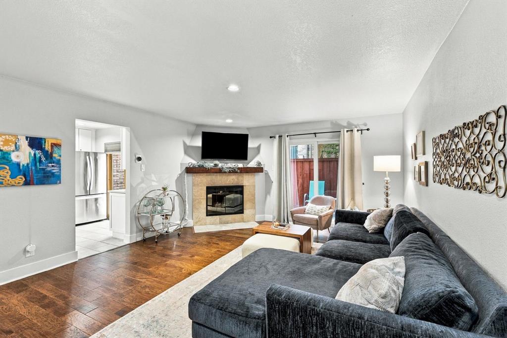 Living area featuring wood-finish flooring, a corner fireplace with stone-tile surround, a rustic wood mantel, recessed lighting, and a sliding glass door