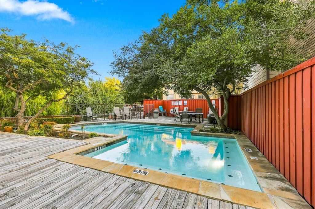Outdoor swimming pool featuring a stone-tile border, wood-finish decking, and perimeter fencing