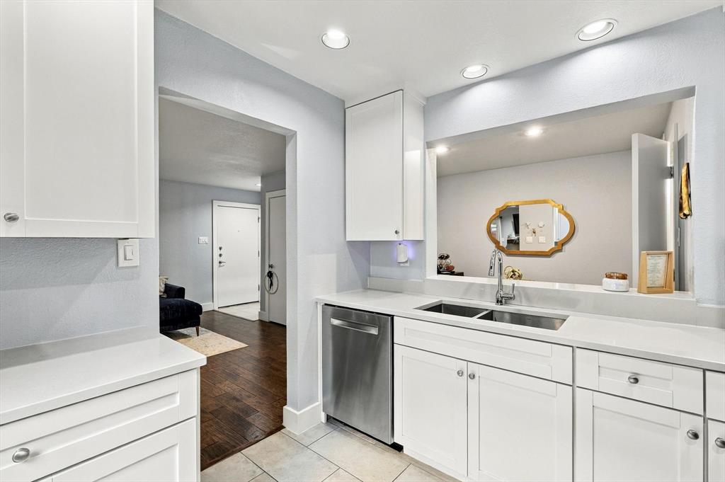 Kitchen featuring white shaker-style cabinetry, solid-surface countertops, stainless steel dishwasher, double-basin undermount sink with chrome gooseneck faucet, and recessed ceiling lighting