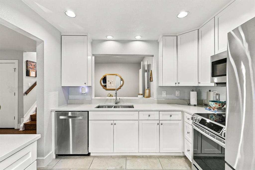 Kitchen featuring white shaker-style cabinetry, stainless steel appliances, solid-surface countertops, dual-basin under-mount sink, and recessed lighting