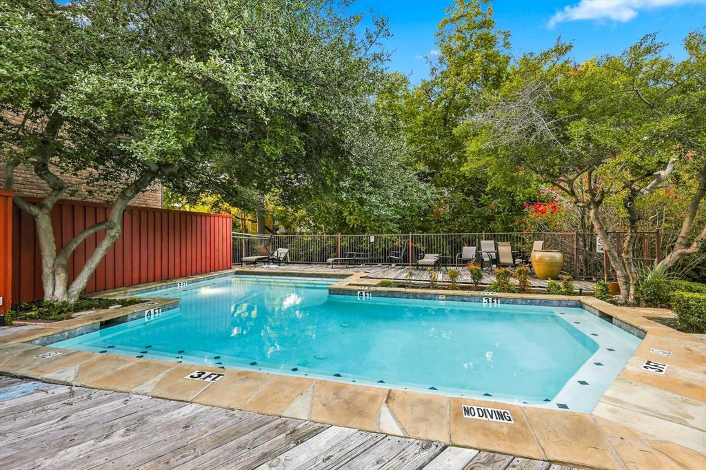 In-ground swimming pool featuring a flagstone coping border, wood-finish decking, vertical privacy fencing, and mature canopy trees