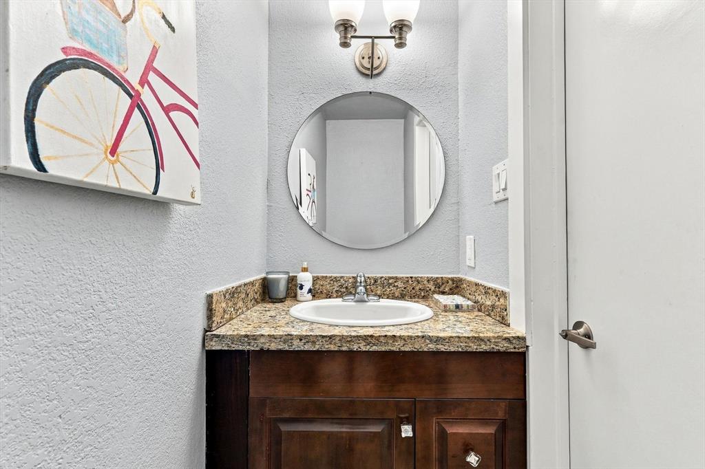 Bathroom featuring a dark wood cabinet, stone-surface countertop with an integrated basin, circular wall-mounted mirror, and dual-bulb overhead lighting