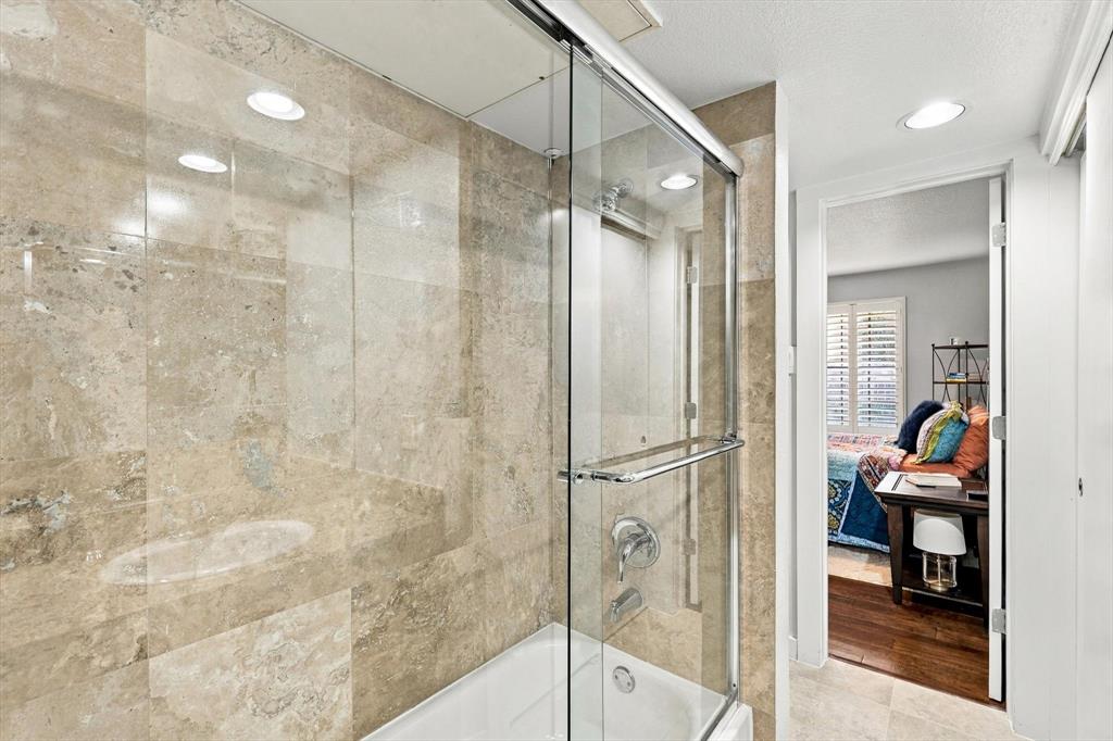 Shower-tub combination featuring floor-to-ceiling stone-finish tile surround, sliding glass enclosure, recessed lighting, and integrated faucet hardware