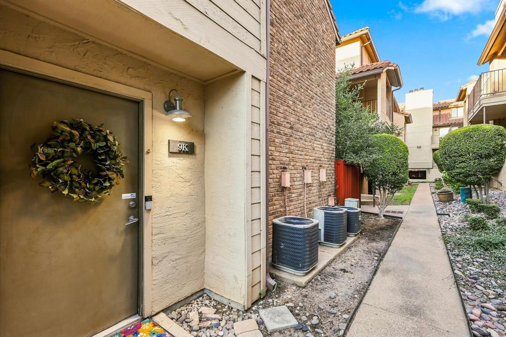 Exterior entry featuring stucco siding, brick veneer accent, wall-mounted gooseneck lighting, and a concrete walkway