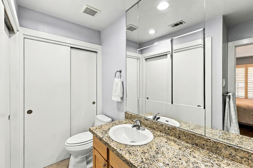 Bathroom vanity featuring a stone-composite countertop, undermount sink, chrome faucet, wood-finish cabinetry, and a full-width wall mirror