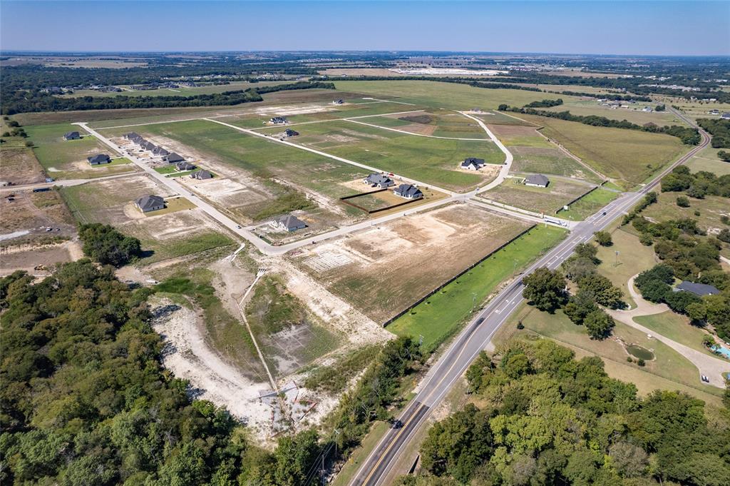 Aerial perspective of a large-scale residential development featuring paved roadway infrastructure, cleared building lots, and perimeter wood-line borders