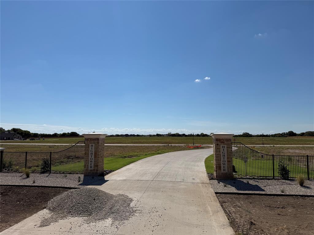 Concrete driveway entrance featuring brick-faced stone pillars and black metal perimeter fencing
