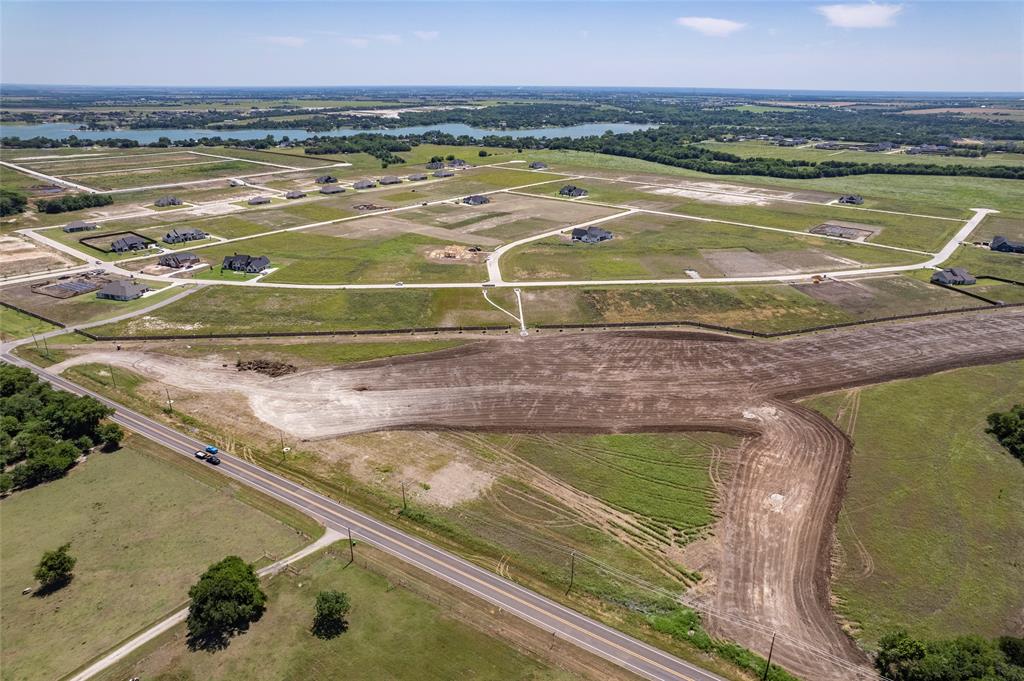 Aerial perspective of expansive residential acreage featuring cleared development sites, paved roadway infrastructure, and water frontage