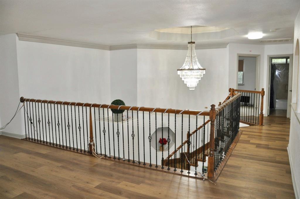 Landing area featuring wood-finish flooring, metal baluster railing with wooden handrails, recessed wall niche, tiered crystal chandelier, and tray ceiling