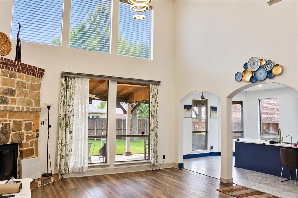 Double-height ceilings with stacked windows, floor-to-ceiling natural stone fireplace, wood-finish flooring, and arched architectural openings