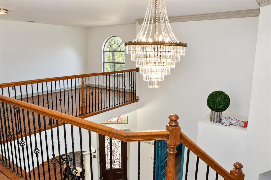 Multi-tiered crystal chandelier featuring a metallic finish, arched window, wood-finish flooring, and metal balustrade with wood handrails