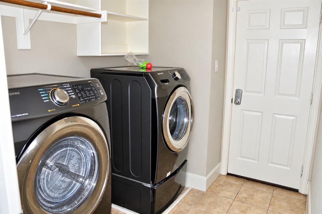 Utility room featuring ceramic tile flooring, built-in white shelving with a hanging rod, and a six-panel door with metal hardware