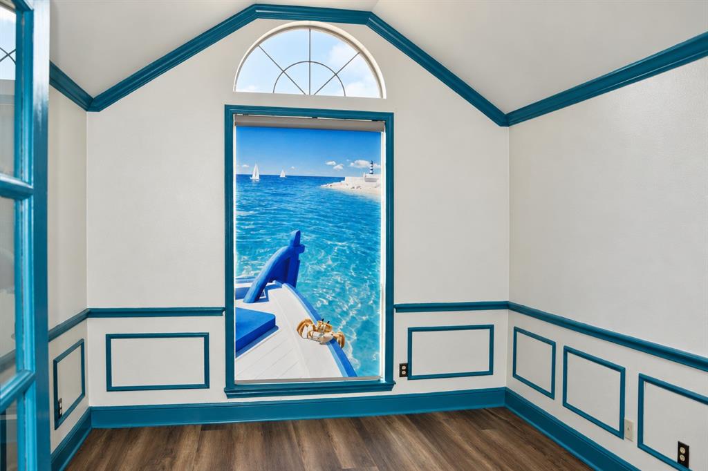 Vaulted ceiling room featuring wainscoting, contrast-color trim, wood-finish flooring, and a semi-circular transom window