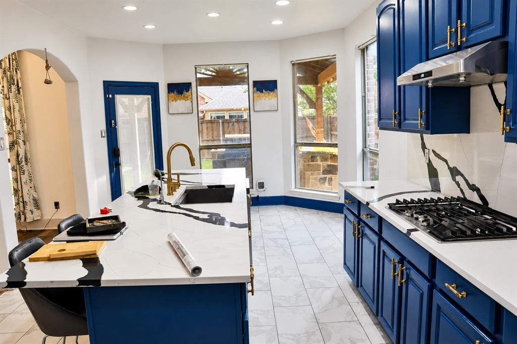 Kitchen featuring blue cabinetry with gold-tone hardware, white countertops with veining, a stainless steel gas cooktop, and tile flooring
